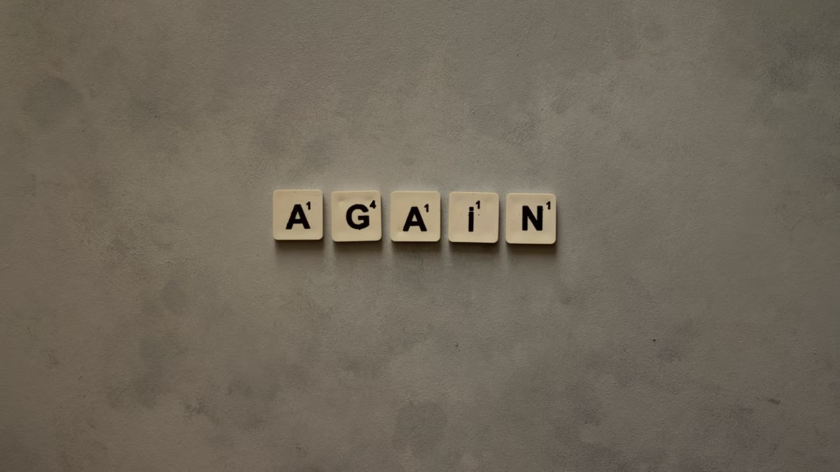 Close-up of Scrabble tiles spelling out 'Again' on a textured background.